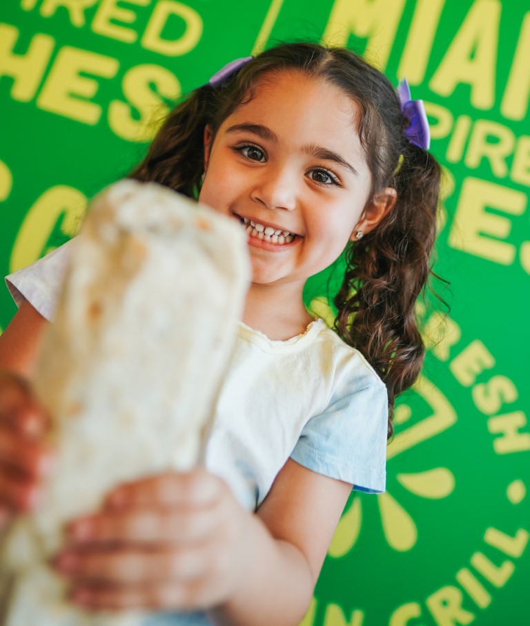 Young girl holds a burrito from LIME Fresh Mexican Grill and smiles