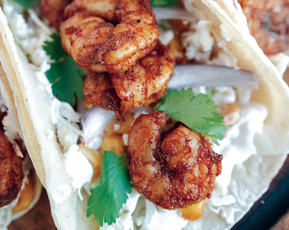 flour taco with spicy shrimp, cabbage, cotija cheese, lime crema, corn and onion